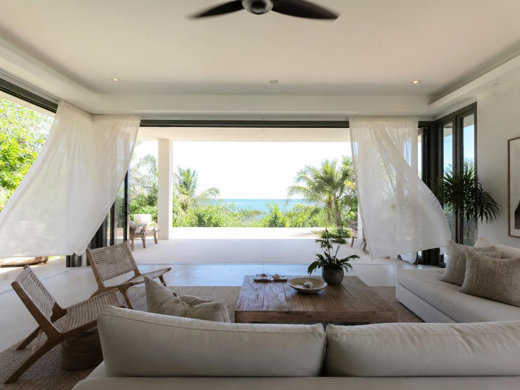 Intérieur lumineux d'une maison tropicale traversée par un courant d'air, voilages soulevés par la brise